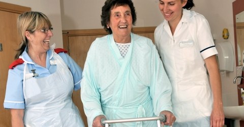 Physiotherapists assisting lady with walking frame.