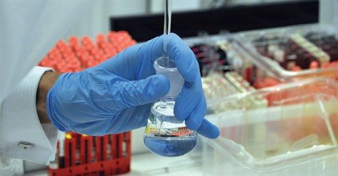 A lab technician wearing blue rubber gloves extracting a liquid sample from a vial.