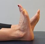 Feet flat on a bed, toes pointing up, toes of one foot flexed towards body
