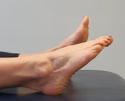 Feet flat on a bed, toes pointing up, toes of one foot pointed away from body