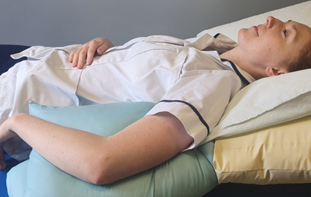 Person shown sleeping on back with a pillow tucked under arm to support injured shoulder 