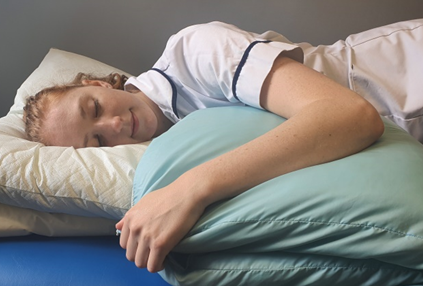 Person shown sleeping on side with a doubled over pillow to support injured shoulder and arm which is on top