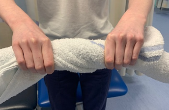 Image shows an individual holding and twisting a rolled up towel 