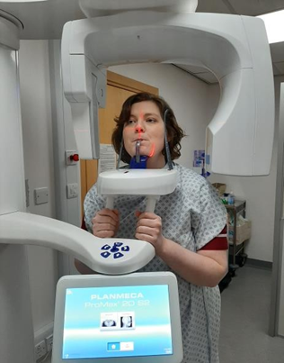 A photo of a person having a teeth x-ray. They are holding special handles on the machine and resting their head and chin in special rests. They are 