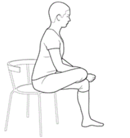 Person is sat on chair with leg crossed on top ankle on knee. Hands hold ankle.