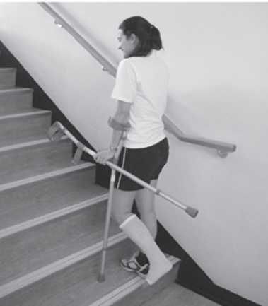 An individual preparing to walk up the next step using one crutch and stair rail but carrying the other crutch whilst holding the usable crutches handle