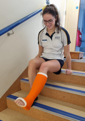 An individual in a leg plaster cast moving up some stairs on their bum. They are using both hands to push themselves up the stairs