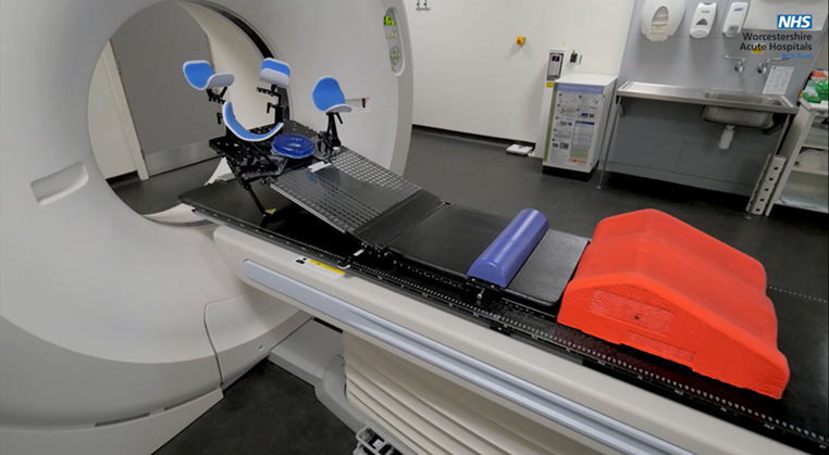 An image of the scanner bed with some equipment that the Radiologists use to help people remain still. Including red knee supports, blue foam supports, stirrups for legs and arms and head rests