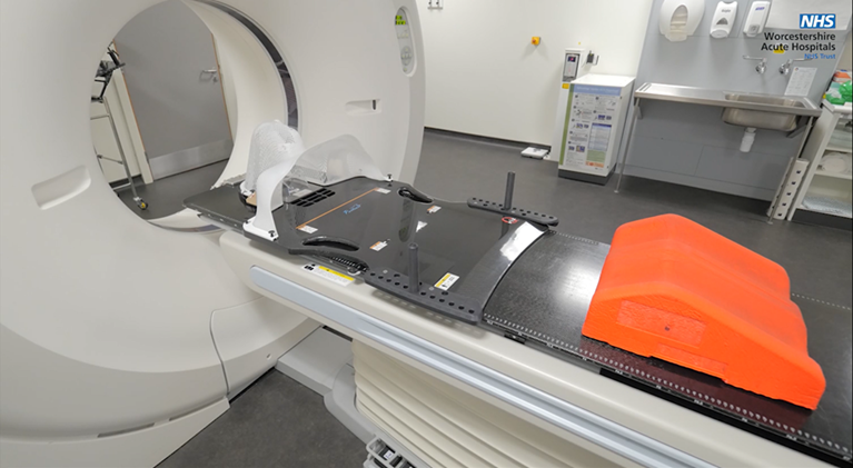 An image of the scanner bed with some equipment that the Radiologists use to help people remain still. Including a red knee support and a body board with a head positioning cradle