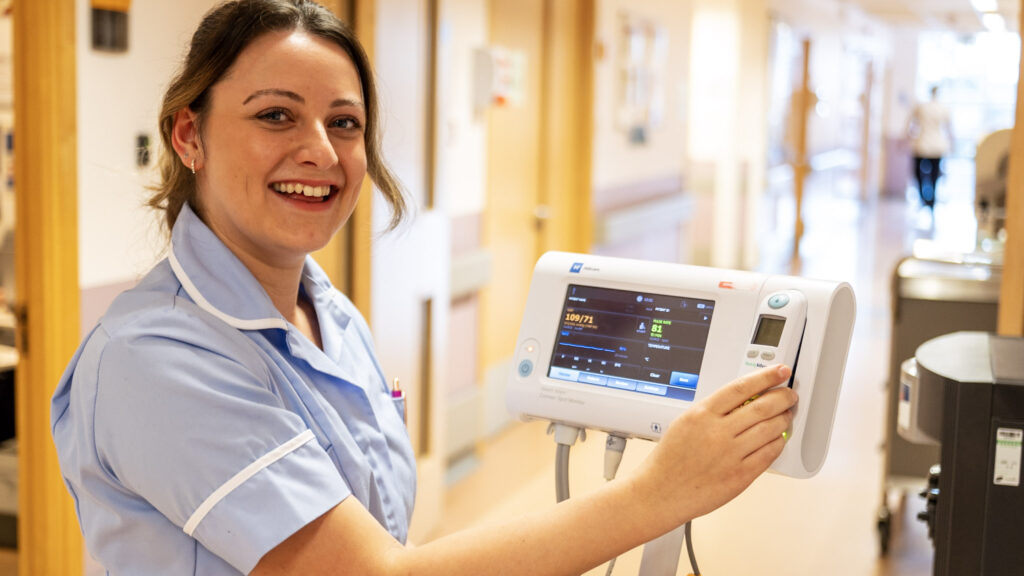 A healthcare assistant smiling at camera while undertaking observations