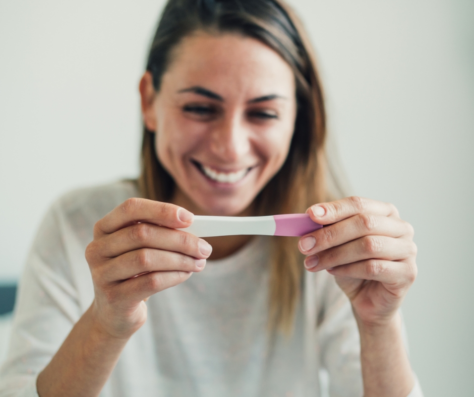 An image of a smiling woman looking at a positive pregnancy test.