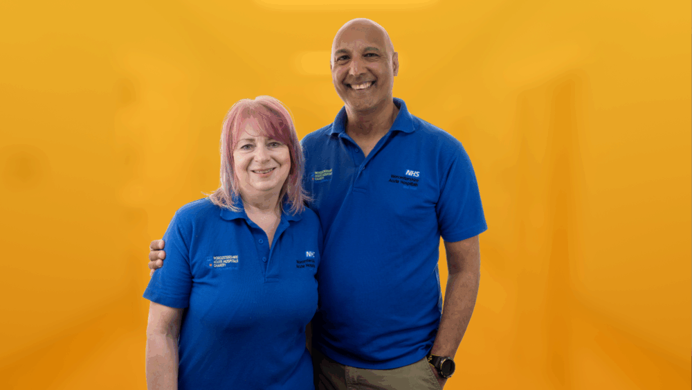 Photo of two volunteers wearing the volunteer t-shirt in front of an orange background.