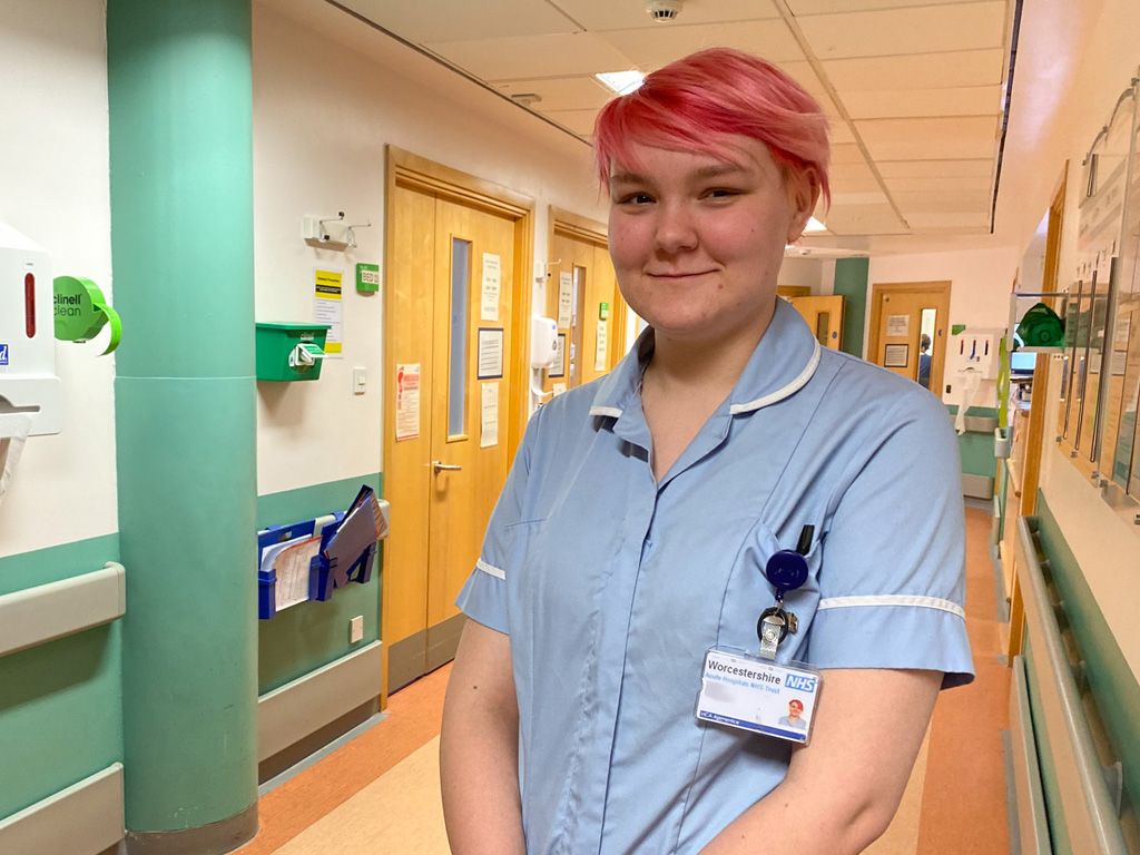 Photograph of a Healthcare Worker standing smiling in hospital corridor. Happy portrait shot.
