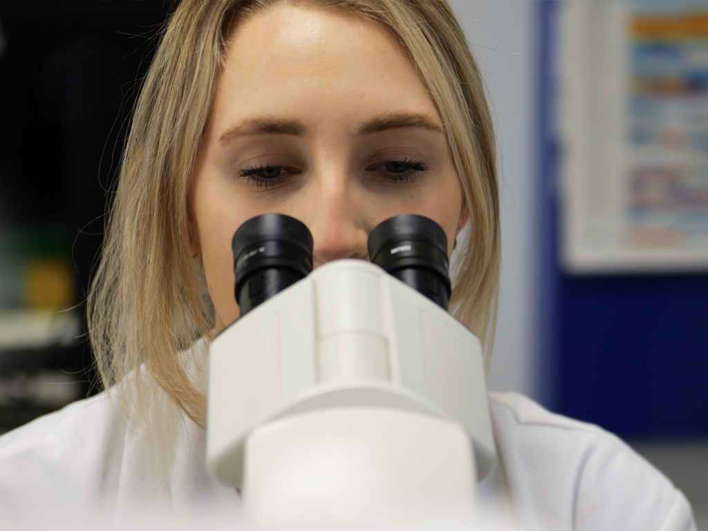 Photograph of a women looking down into a microscope.
