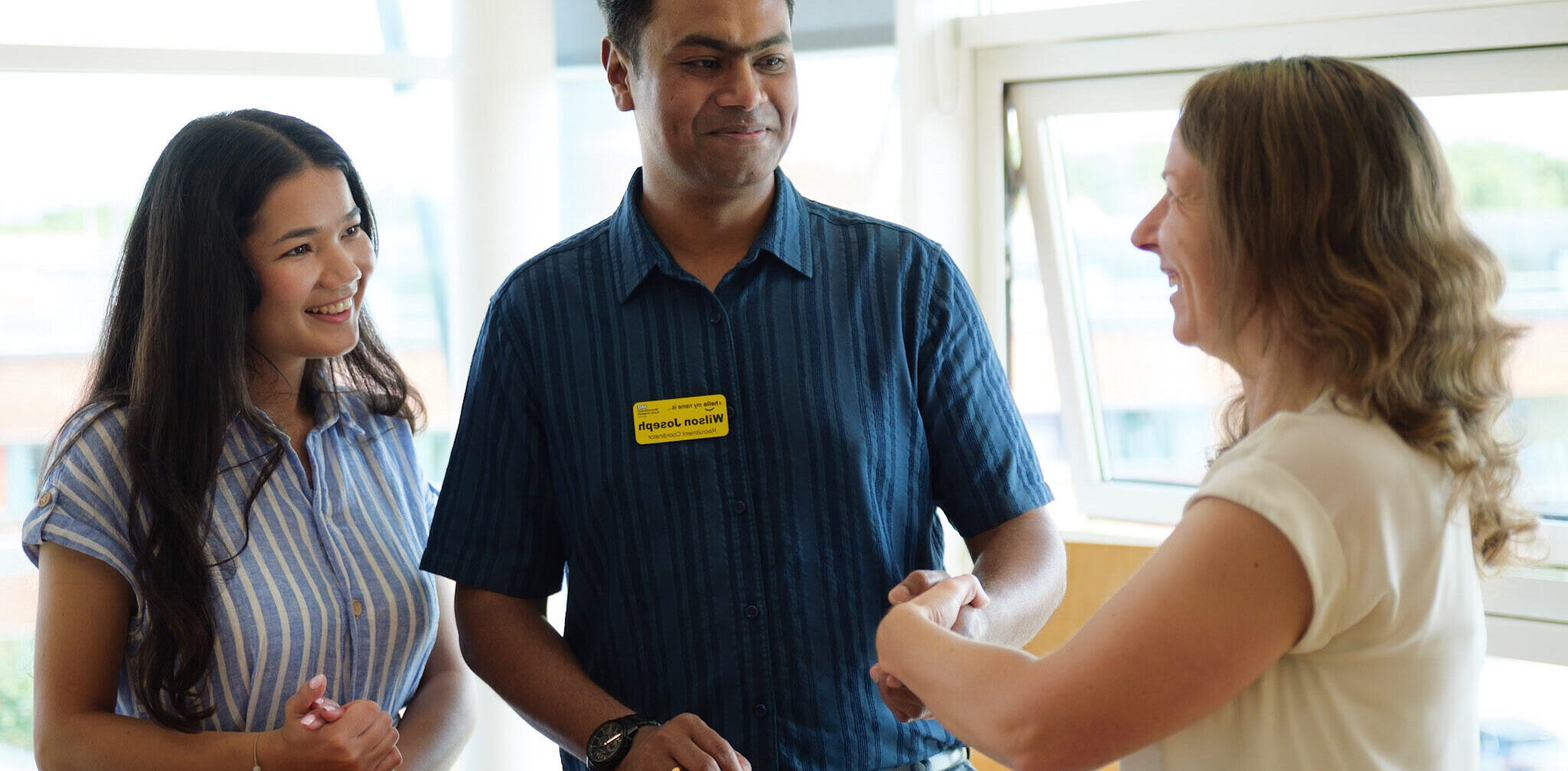 Two members of the recruitment team, with one colleague shaking hands with another person.