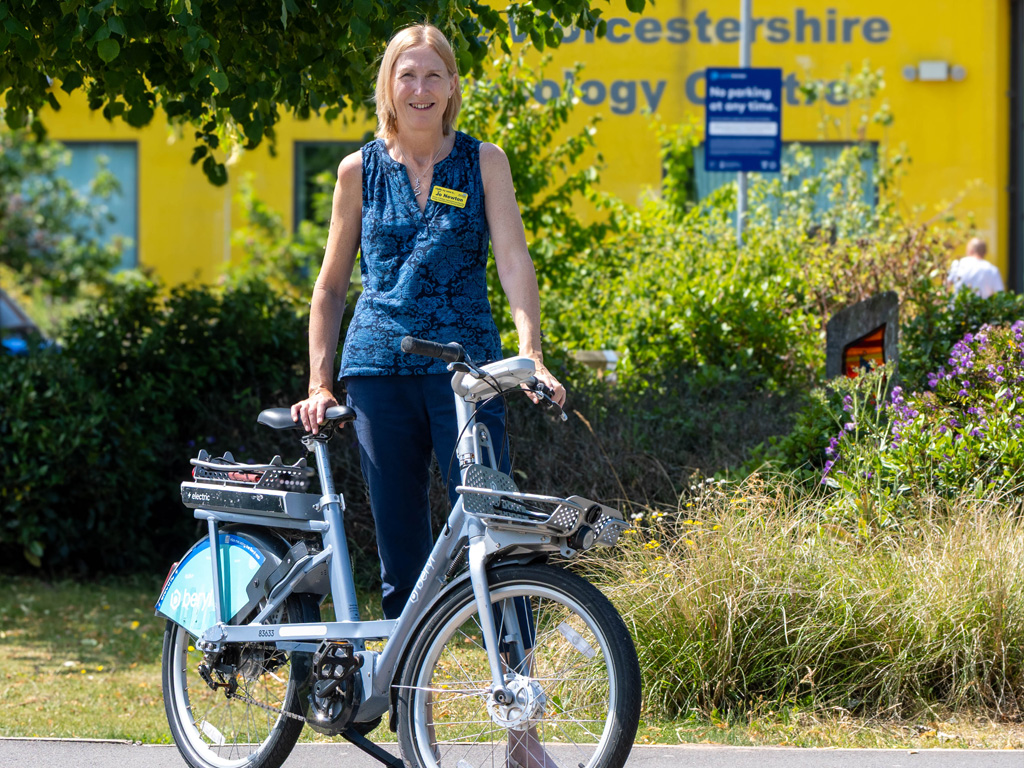 photo of female member of staff standing outside Worcestershire Acute Hospitals NHS holding an electric bike.