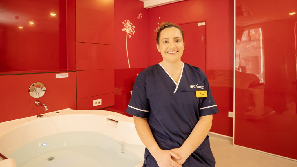 A midwife sat on the edge of a bathtub in a birthing suite.