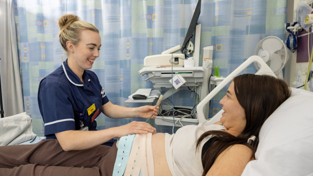 A midwife observing a pregnant woman in a hospital assessment bed.