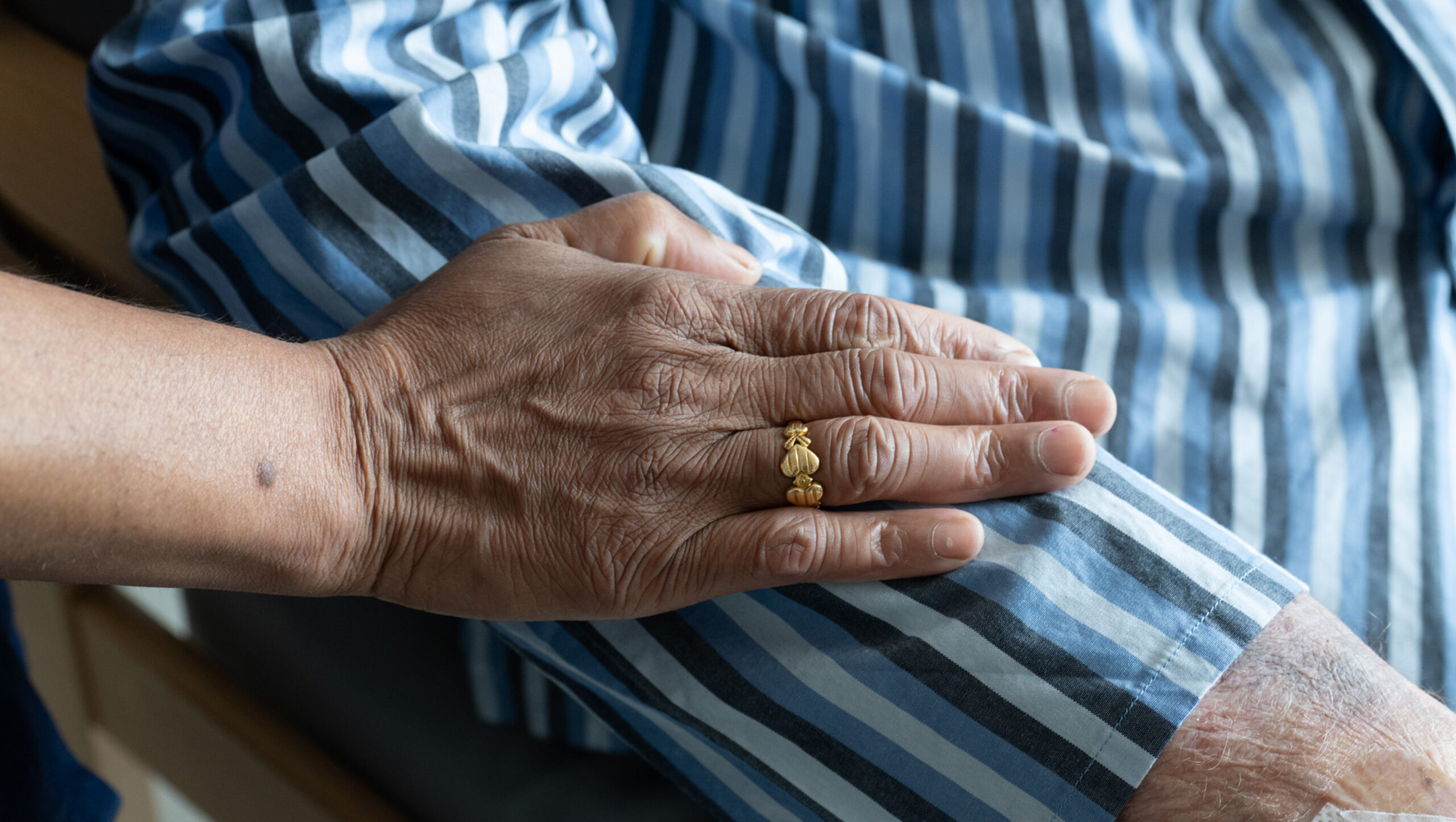 Close-up photograph of a hand resting gently on the arm of a patient wearing pinstriped pyjamas.