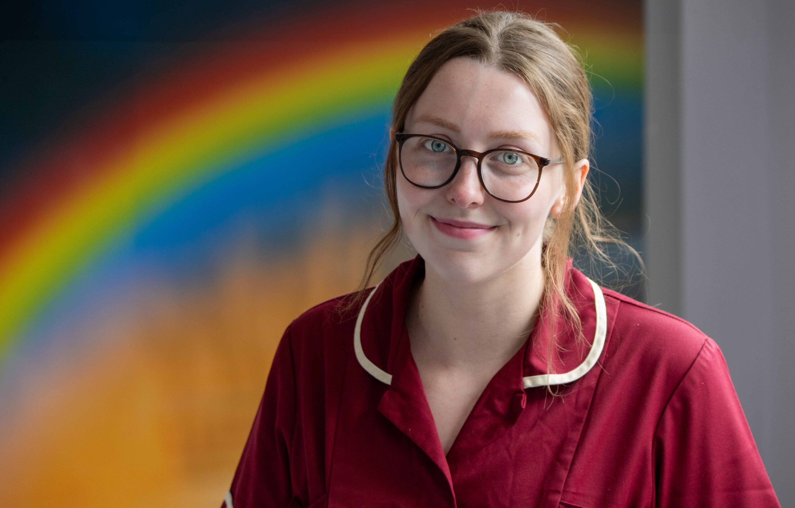 Dietitian smiling at the camera,. A rainbow picture is visible in the background