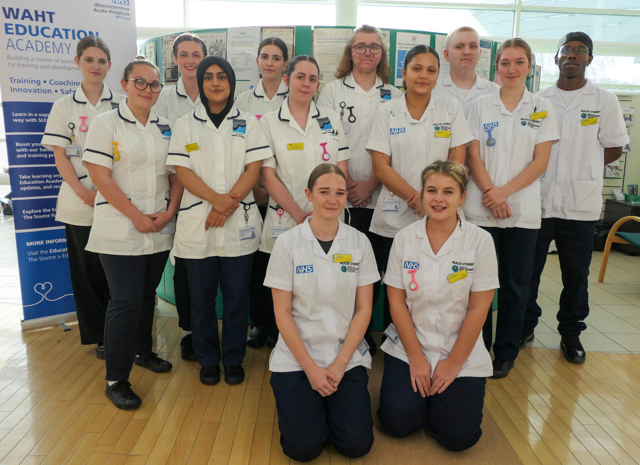 A group of T-Level students in white healthcare uniforms pose for a photo in a hospital reception.