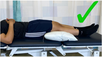 A do image with a green tick showing an individual lay on back with knees supported by a pillow under them