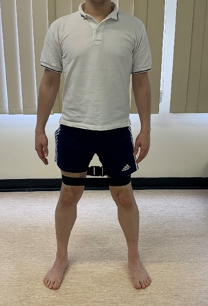 Image shows individual stood with a belt looped and fastened just above the knees. Feet are just over shoulder width apart