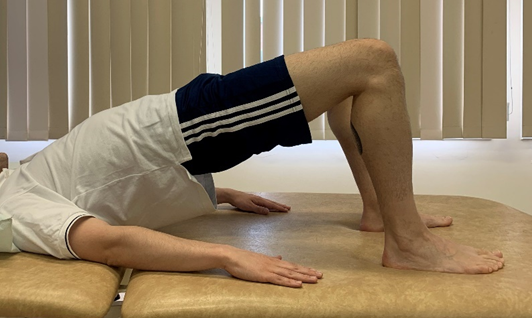 Image shows an individual in bridge pose with feet upper body, head and arms flat on floor and hips pushed up towards the ceiling