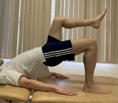 Image shows an individual in bridge pose with a foot, upper body, head and arms flat on floor and hips pushed up towards the ceiling. One leg is off the floor and bent