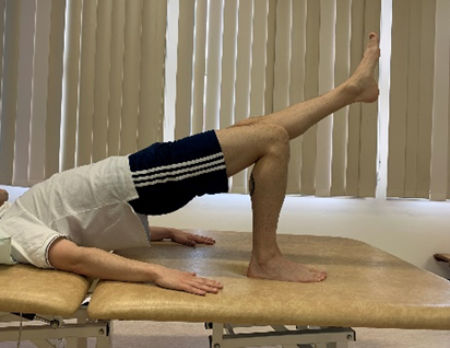 Image shows an individual in bridge pose with a foot, upper body, head and arms flat on floor and hips pushed up towards the ceiling. One leg is off the floor and straight