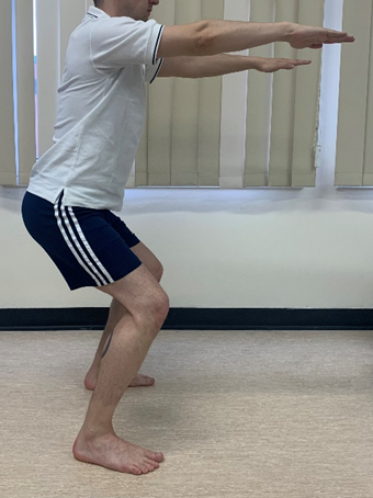 Image shows an individual in a small squat. Arms are held straight out in front and knees are slightly bent over toes