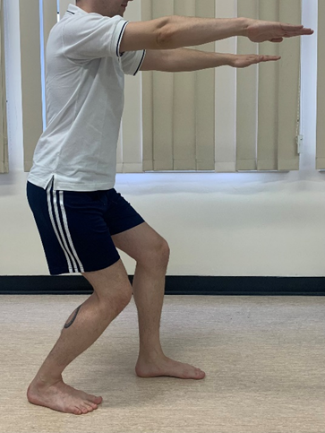 Image shows an individual in a squat. Arms are held straight out in front and knees are slightly bent over toes. One leg is a pace length in front of the other