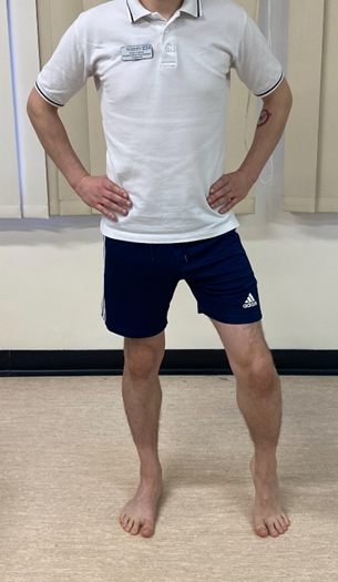 Image shows an individual stood on a hard floor with hands on hips. Feet a waist with apart and heel of one foot is raised