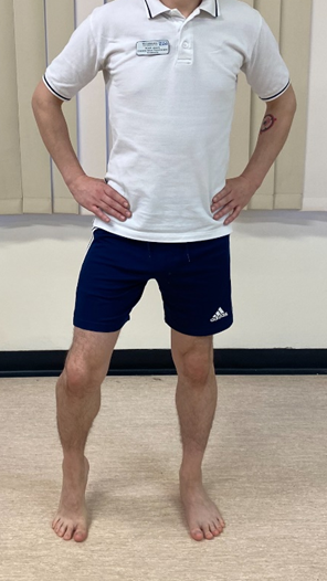 Image shows an individual stood on a hard floor with hands on hips. Feet a waist with apart and heel of one foot is raised