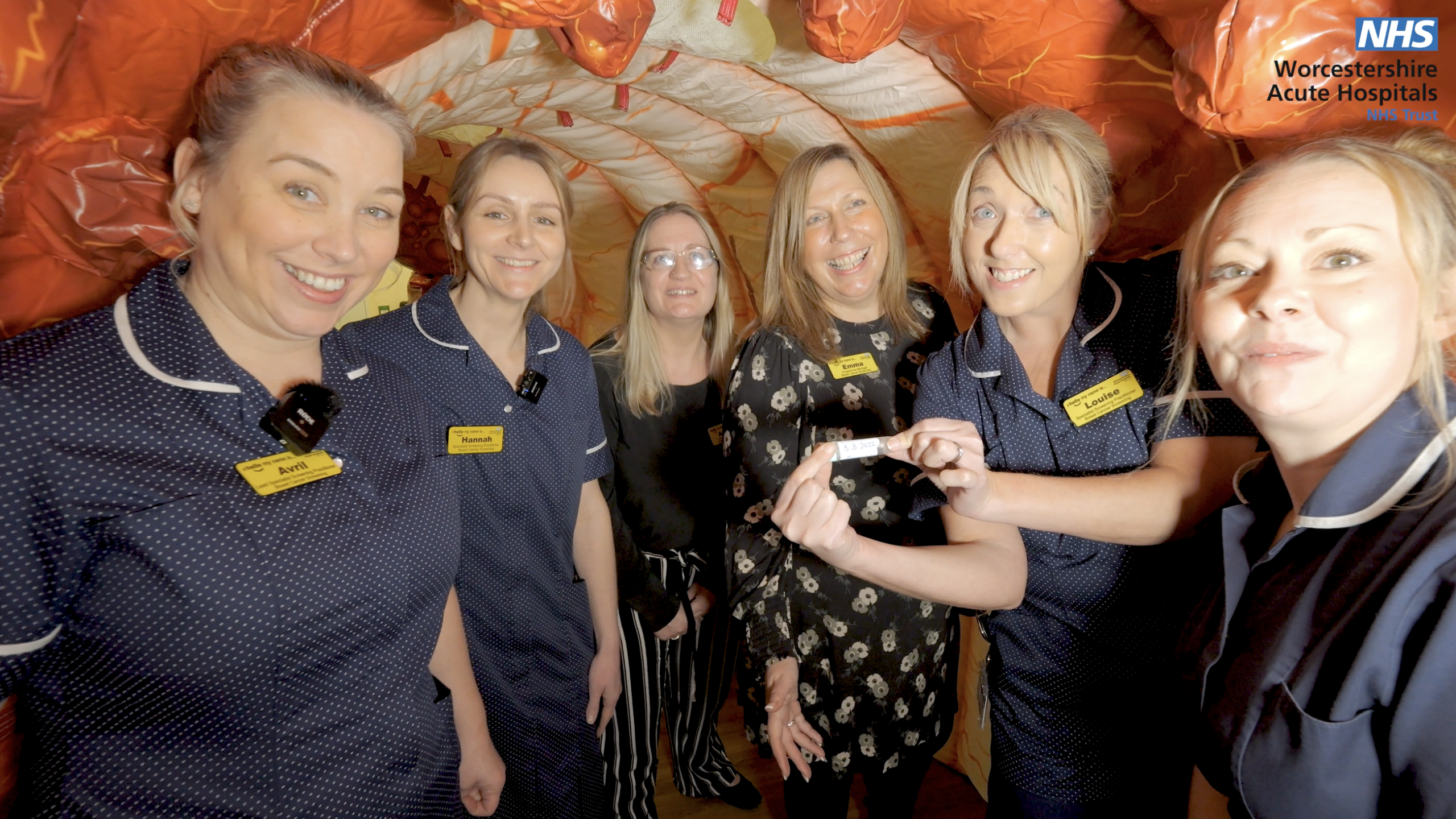 An image of the bowel cancer screening team in uniform, stood at the entrance of a giant inflatable bowel.