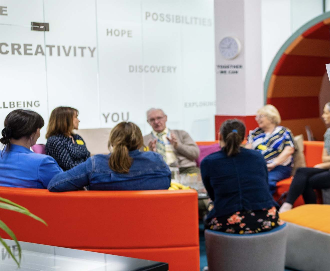 Photograph of volunteers in the Co-Lab at Kidderminster Hospital. Chatting on seats.