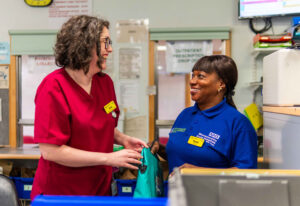 Photograph of Discharge Response Volunteer smiling and talking to pharmacist in a hospital setting. 