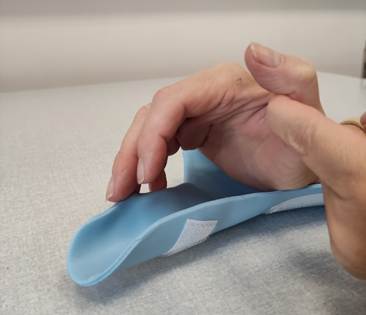 A picture of a persons hand in a splint, lifting the wrist off the splint using the non-affected hand