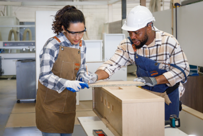 A picture of a person working alongside another person making a cabinet