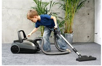 A photograph of a boy next to a hoover pressing the button to start it.