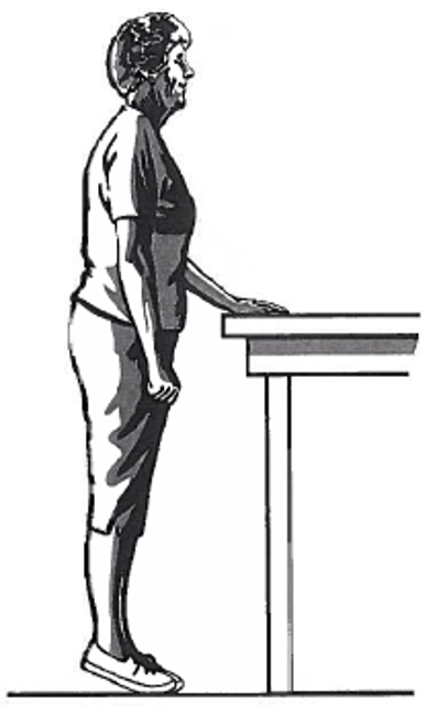 Picture of a person standing next to a table, holding onto the surface with one hand whilst coming up onto the toes