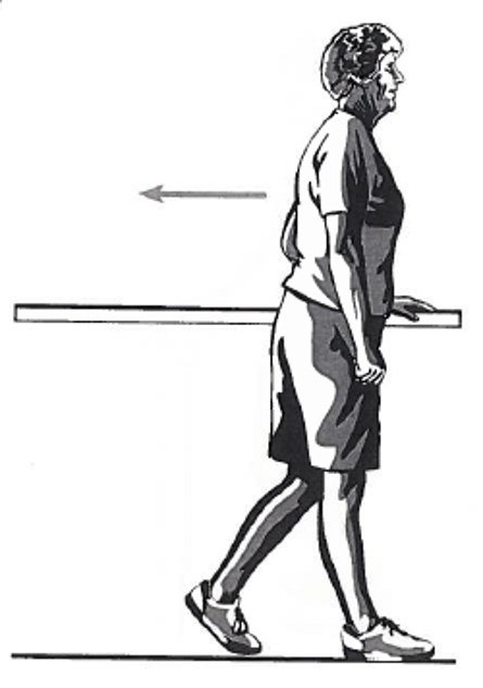 Picture of a person standing sideways next to a table, holding onto the surface with one hand whilst walking backwards