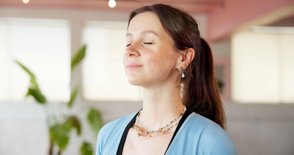 Woman in meditation at home with windows and a plant in the background.